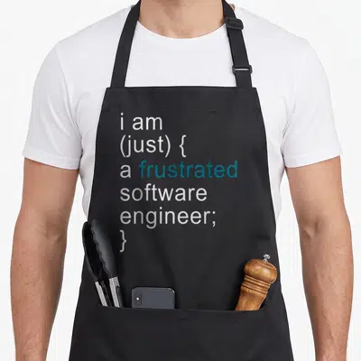 Tablier de cuisine noir avec le texte « i am (just) { a frustrated software engineer; } » en typographie code source.