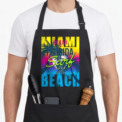 Tablier de cuisine noir avec un graphisme coloré Miami Beach Florida Surf Club et palmiers.