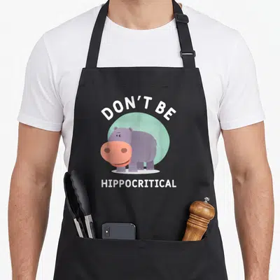 Tablier de cuisine noir avec illustration d'hippopotame violet et texte Don't Be Hippocritical en blanc.