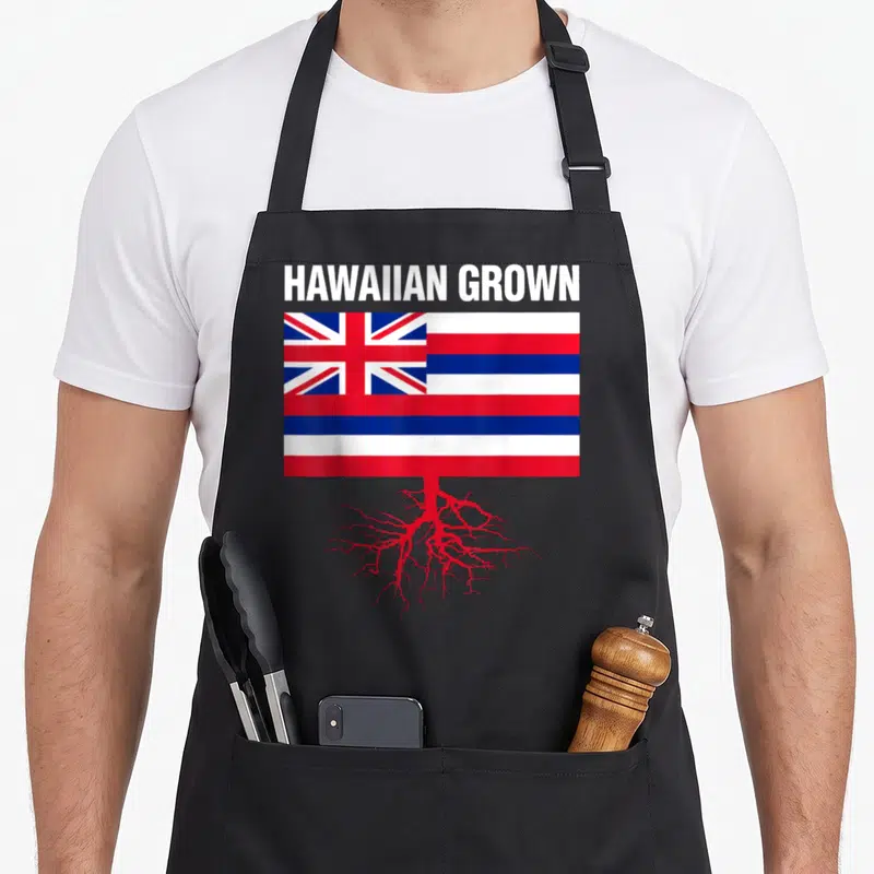 Tablier de cuisine noir avec illustration du drapeau hawaïen surmonté de racines rouges et du texte HAWAIIAN GROWN en blanc.