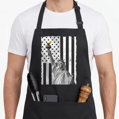 Tablier de cuisine noir avec Statue de la Liberté et drapeau américain en noir et blanc et flamme dorée.