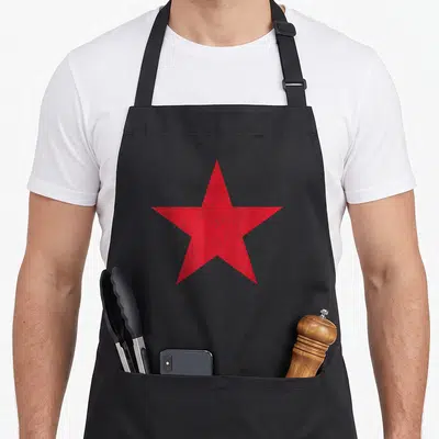 Tablier de cuisine noir avec une grande étoile rouge à cinq branches au centre, effet vieilli et texturé.