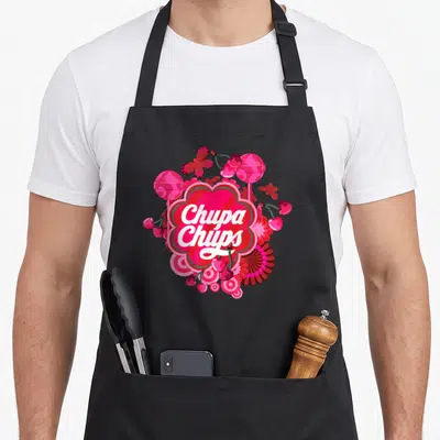 Tablier de cuisine noir avec le logo Chupa Chups et des illustrations de bonbons roses et de fleurs stylisées.
