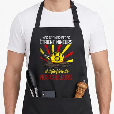 Tablier de cuisine noir avec casque de mineur jaune, pioche et texteNos grands-pères étaient mineurs et déjà fiers de nos couleurs.