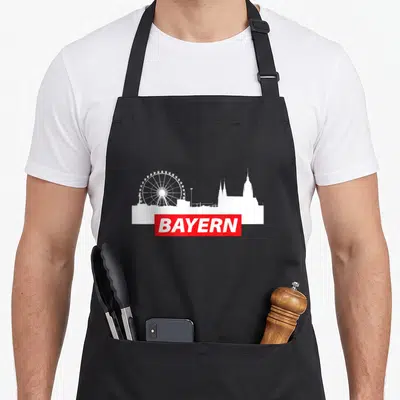 Tablier de cuisine noir avec silhouette blanche de Munich, grande roue et bande rouge portant le mot BAYERN