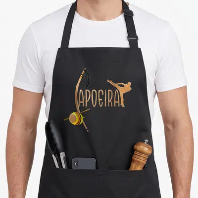 Tablier de cuisine noir avec illustration dorée d'un berimbau et la silhouette d'un pratiquant de capoeira en mouvement dynamique.