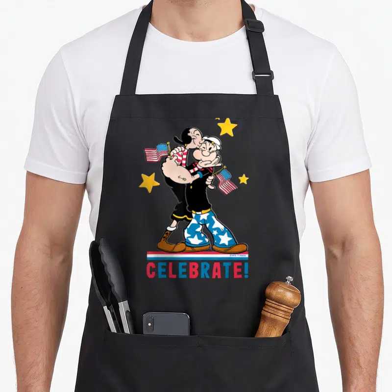 Tablier de cuisine noir avec Popeye et Olive Oyl tenant des drapeaux américains sous le texte CELEBRATE.