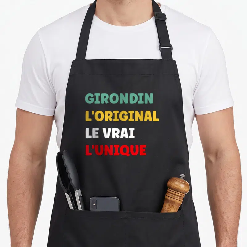 Tablier de cuisine noir avec inscription multicolore GIRONDIN L'ORIGINAL LE VRAI L'UNIQUE centrée sur le devant.