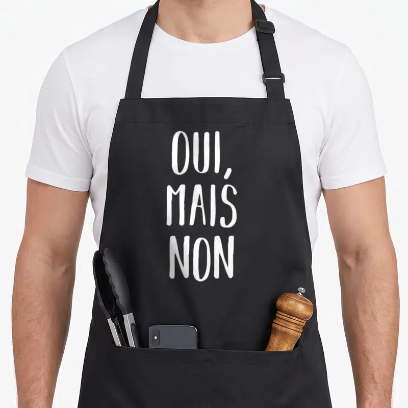 Tablier de cuisine noir avec l'inscription blanche OUI, MAIS NON en lettres capitales manuscrites.