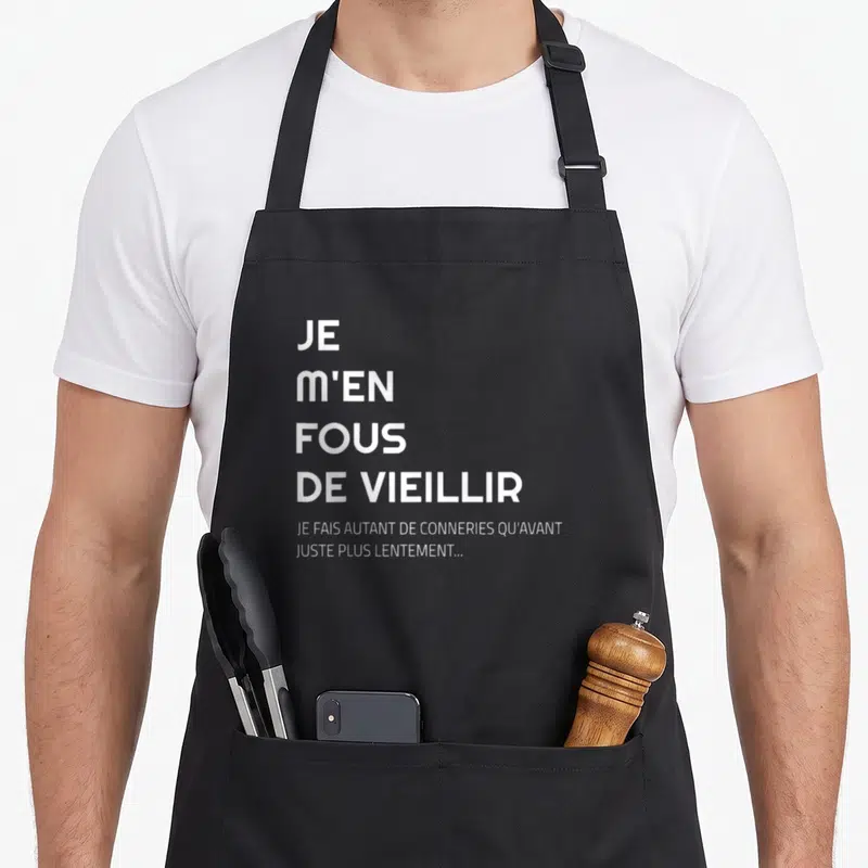 Tablier de cuisine noir avec le texte blanc Je m'en fous de vieillir et je fais autant de conneries qu'avant juste plus lentement.
