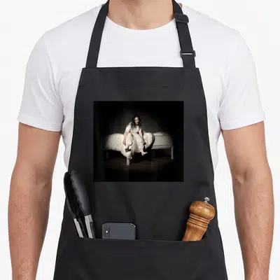 Tablier de cuisine noir avec une illustration de Billie Eilish assise sur un lit blanc dans une pièce sombre.