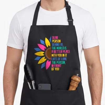 Tablier de cuisine noir avec une fleur stylisée multicolore et un message d'espoir imprimé en lettres vives.