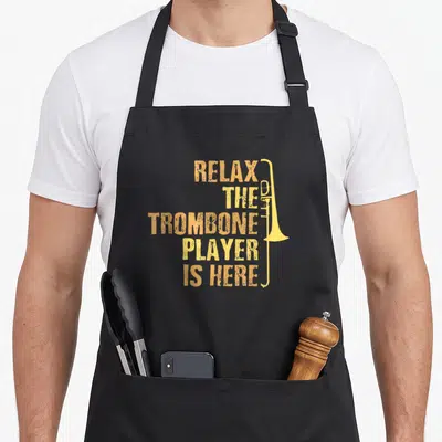 Tablier de cuisine noir avec texte Relax the Trombone Player Is Here et illustration de trombone jaune doré.