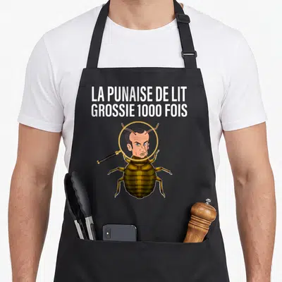 Tablier de cuisine noir avec illustration d'une punaise de lit au visage humain sous loupe et texte blanc en haut.
