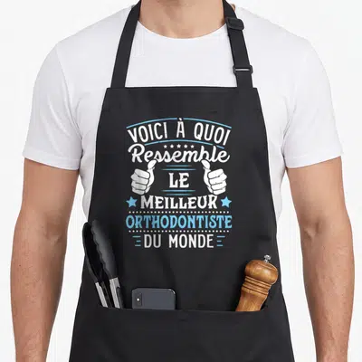 Tablier de cuisine noir avec inscription Voici à quoi ressemble le meilleur orthodontiste du monde et deux mains faisant un pouce levé.