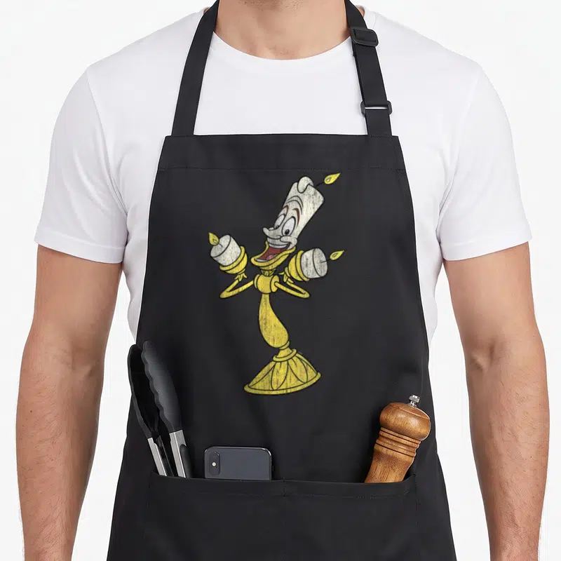 Tablier de cuisine noir avec illustration colorée et texturée du bougeoir Lumière souriant aux bras ouverts.