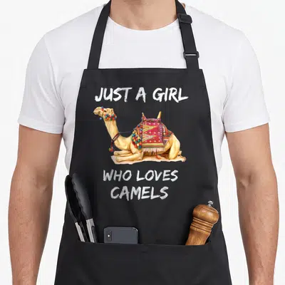 Tablier de cuisine noir avec illustration d'un chameau assis orné de pompons et d'une selle colorée sous le texte Just a girl who loves camels.