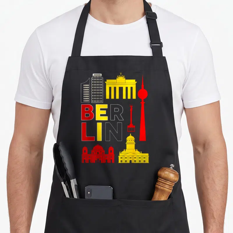 Tablier de cuisine noir avec un graphisme coloré représentant les monuments de Berlin et le nom BERLIN en lettres stylisées.