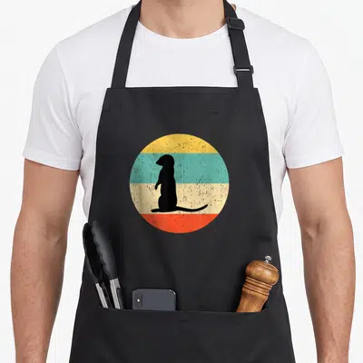 Tablier de cuisine noir avec une silhouette de suricate debout sur un cercle aux bandes jaunes, bleues, crème et orange.