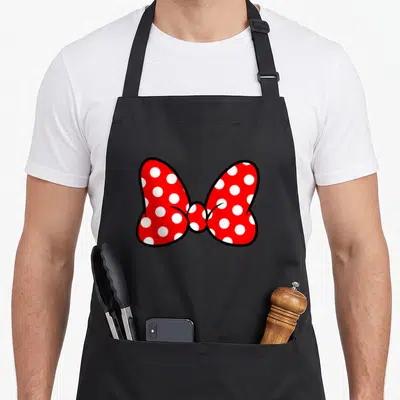 Tablier de cuisine noir avec un grand nœud papillon rouge orné de pois blancs stylisés.