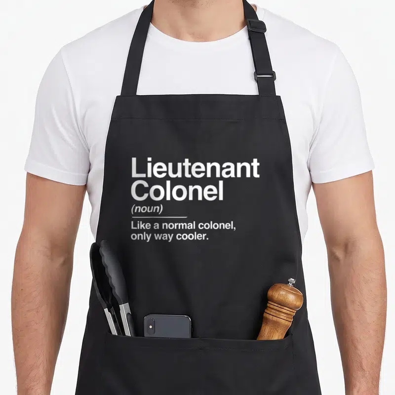 Tablier de cuisine noir avec le texte blanc Lieutenant Colonel Like a normal colonel only way cooler imprimé au centre.