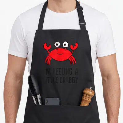 Tablier de cuisine noir avec un crabe rouge dessiné et le texte I'm Feeling A Little Crabby en dessous.