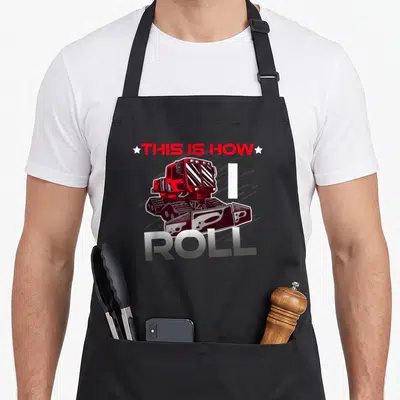 Tablier de cuisine noir avec illustration de Pistenbully rouge et texte This Is How I Roll en lettres métalliques.