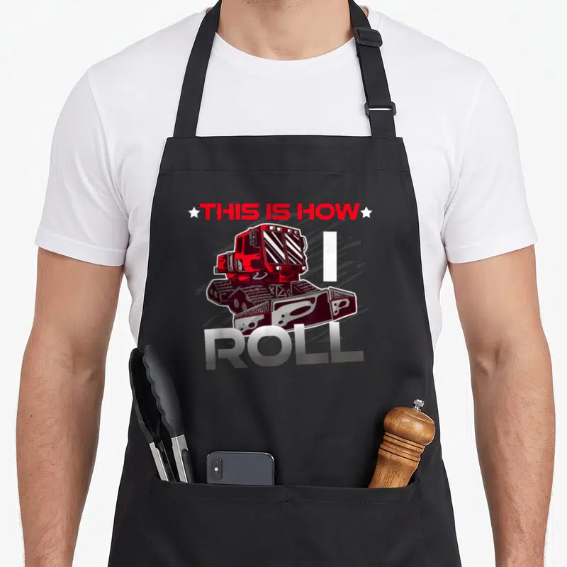 Tablier de cuisine noir avec illustration de Pistenbully rouge et texte This Is How I Roll en lettres métalliques.