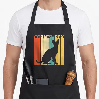Tablier de cuisine noir avec silhouette de chat Cornish Rex sur fond de bandes colorées verticales orange, jaune et turquoise.