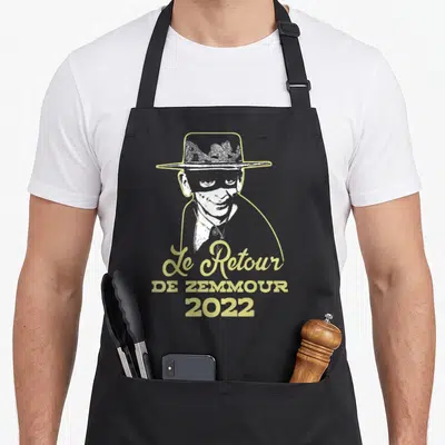 Tablier de cuisine noir avec portrait stylisé d'un homme au chapeau et texte jaune « Le Retour de Zemmour 2022 ».