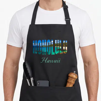 Tablier de cuisine noir avec le mot Honolulu rempli d'une plage et de l'océan turquoise, Hawaii en dessous.