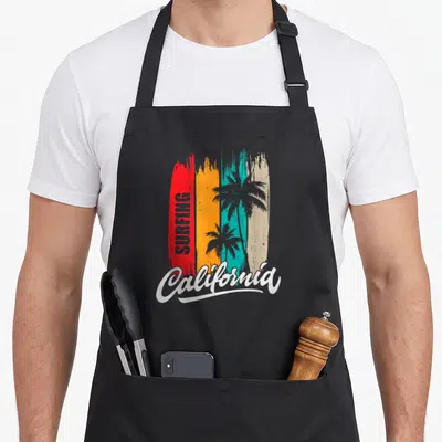 Tablier de cuisine noir avec inscription Surfing California et silhouettes de palmiers sur fond de bandes colorées verticales.