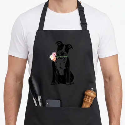 Tablier de cuisine noir avec illustration d'un American Staffordshire Terrier tenant des fleurs dans la bouche.