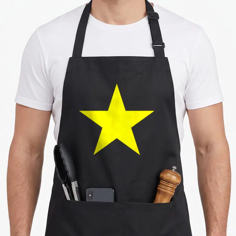 Tablier de cuisine noir avec une grande étoile jaune à cinq branches imprimée au centre du torse.