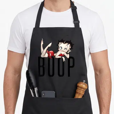 Tablier de cuisine noir avec illustration de Betty Boop allongée sur le texte BOOP en lettres capitales noires.