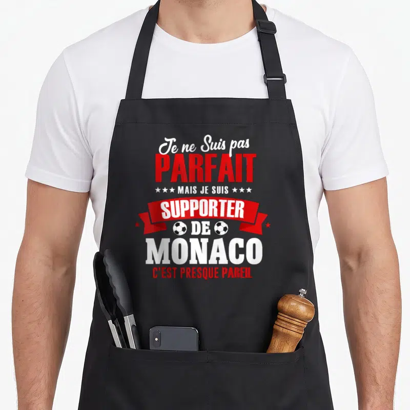 Tablier de cuisine noir avec inscription humoristique sur supporteur de Monaco et deux petits ballons de foot rouges et blancs.