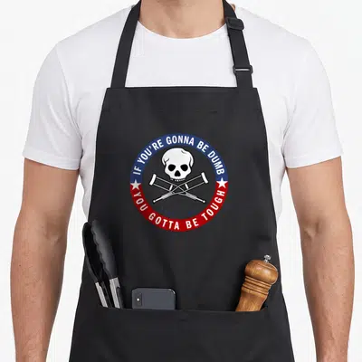 Tablier de cuisine noir avec un logo circulaire montrant un crâne et deux béquiles croisées sur fond gris.