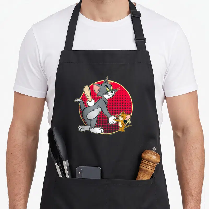 Tablier de cuisine noir avec Tom tenant une batte de baseball et Jerry souriant devant un fond rouge à pois.
