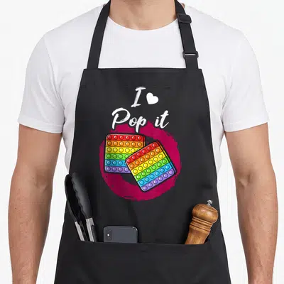 Tablier de cuisine noir avec deux pop it multicolores et le texte blanc I Love Pop it sur fond rose vif.