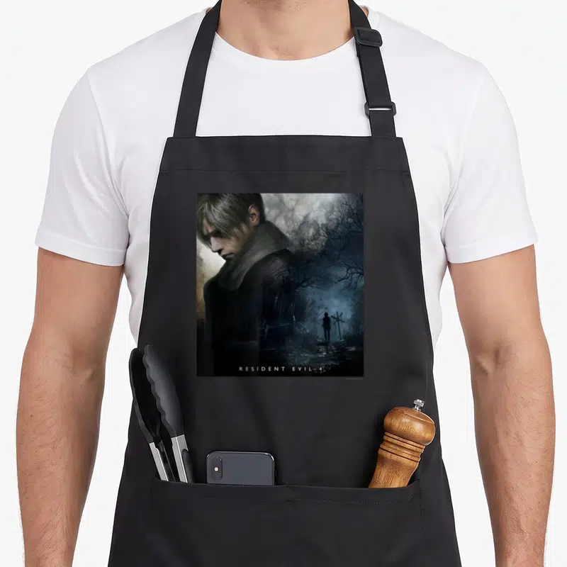 Tablier de cuisine noir avec portrait de Leon S. Kennedy et silhouette dans un paysage brumeux du jeu Resident Evil 4.