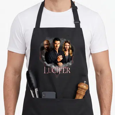 Tablier de cuisine noir avec une illustration des personnages de la série Lucifer et leur nom en lettres stylisées rouges.