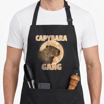 Tablier de cuisine noir avec illustration de capybara et texte CAPYBARA GANG en lettres capitales orange.
