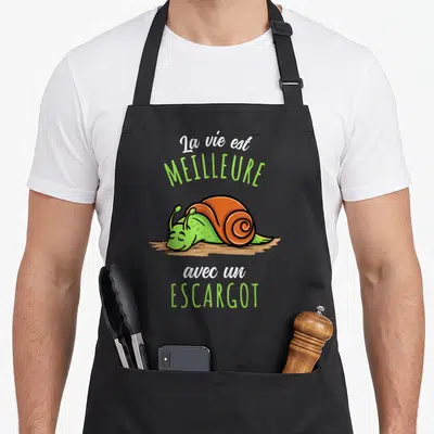 Tablier de cuisine noir avec illustration d'escargot souriant et texte blanc et vert sur fond uni.
