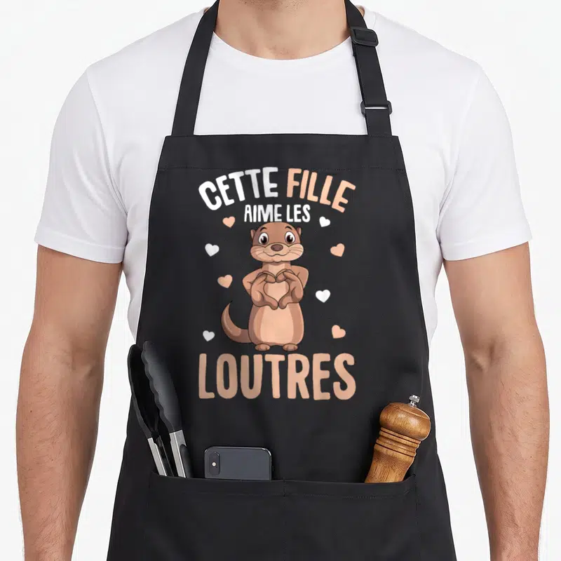Tablier de cuisine noir avec une loutre marron formant un cœur avec ses pattes et des cœurs flottants autour.