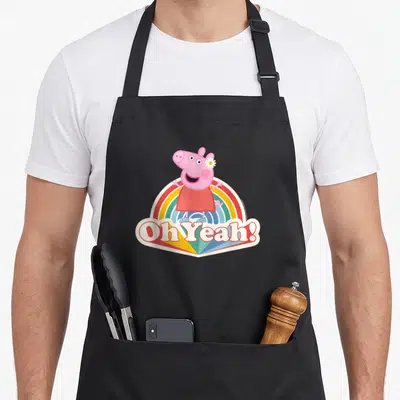 Tablier de cuisine noir avec Peppa Pig souriante sur un arc-en-ciel et le texte Oh Yeah imprimé en bas.