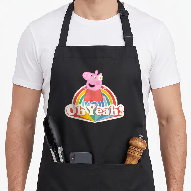 Tablier de cuisine noir avec Peppa Pig souriante sur un arc-en-ciel et le texte Oh Yeah imprimé en bas.