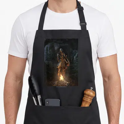 Tablier de cuisine noir avec illustration d'un chevalier en armure se tenant devant un feu de camp dans un paysage forestier sombre et ruiné.
