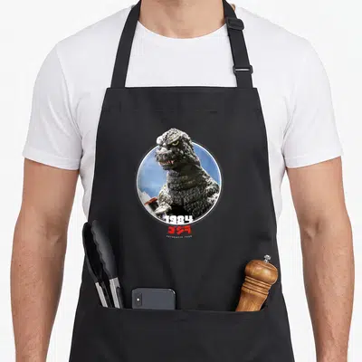 Tablier de cuisine noir avec une illustration circulaire de Godzilla 1984 sur fond bleu et texte Icons of Toho en bas.