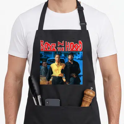 Tablier de cuisine noir avec l'affiche Boyz N The Hood montrant trois hommes et un titre rouge stylisé.