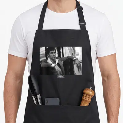 Tablier de cuisine noir avec portrait noir et blanc d'un homme en costume assis et le mot Scarface en bas.